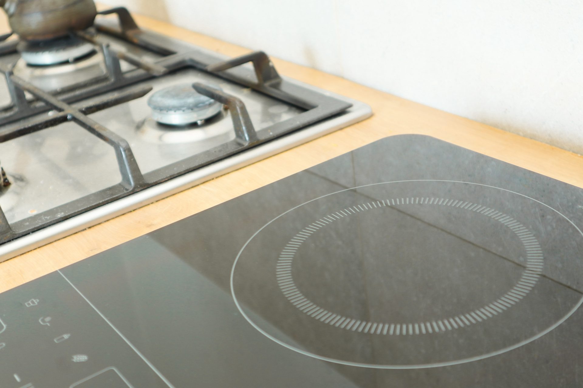 Gas cooktop burners beside an induction cooktop on a timber kitchen bench